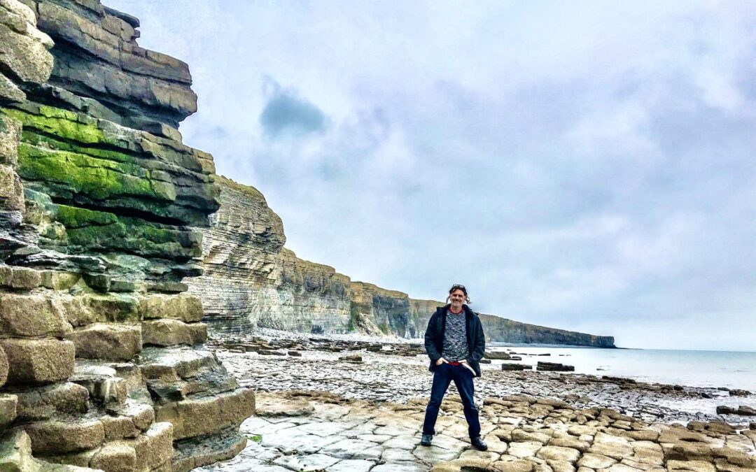 Man met links rotsen en rechts de zee in Wales